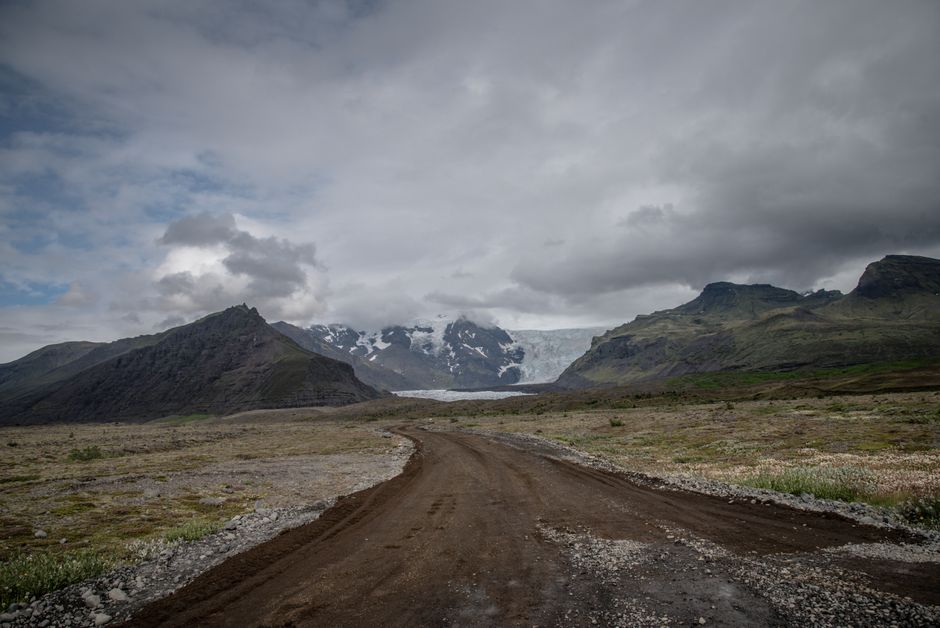 Stunning view of Icelandic mountains and glacier under cloudy skies with an unpaved road.